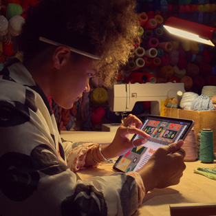 บุคคลหนึ่งนั่งอยู่ที่โต๊ะโดยกำลังใช้นิ้วสองนิ้วซูมภาพบนหน้าจอ iPad