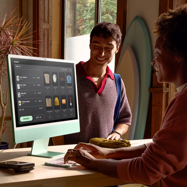 在一家售賣滑浪板和其他產品的店舖，一名員工坐在收銀櫃檯前使用 iMac，為櫃檯另一邊的顧客結帳。