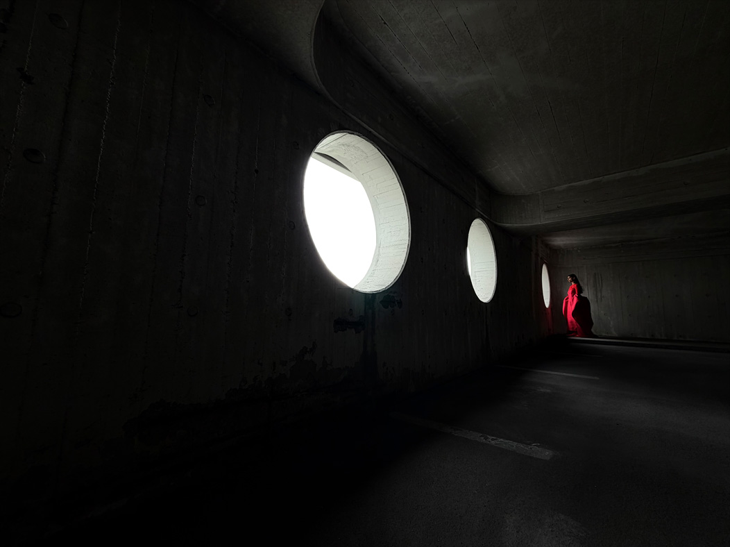 Una mujer con un largo vestido rojo de pie en medio de una habitación vacía mientras la fotografían. La app Fotos alterna entre varias distancias focales para mostrar las capacidades del sistema de cámaras Pro: 200 mm, 100 mm, 48 mm, 35 mm, 28 mm, 13 mm y macro