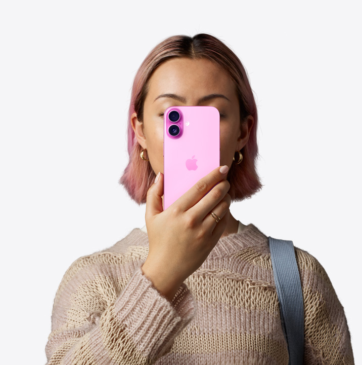 En person håller en iPhone 16 i rosa finish framför ansiktet så att mobilens baksida syns, dubbelkamerasystem längst uppe till vänster.