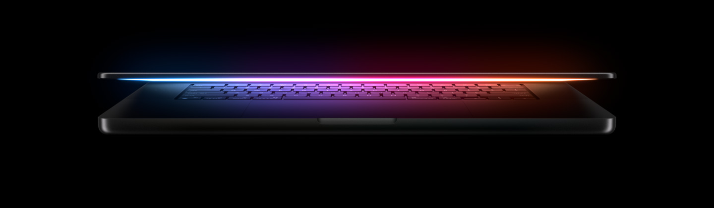 A slightly open MacBook Pro casts a multicolored glow from the screen onto the keyboard